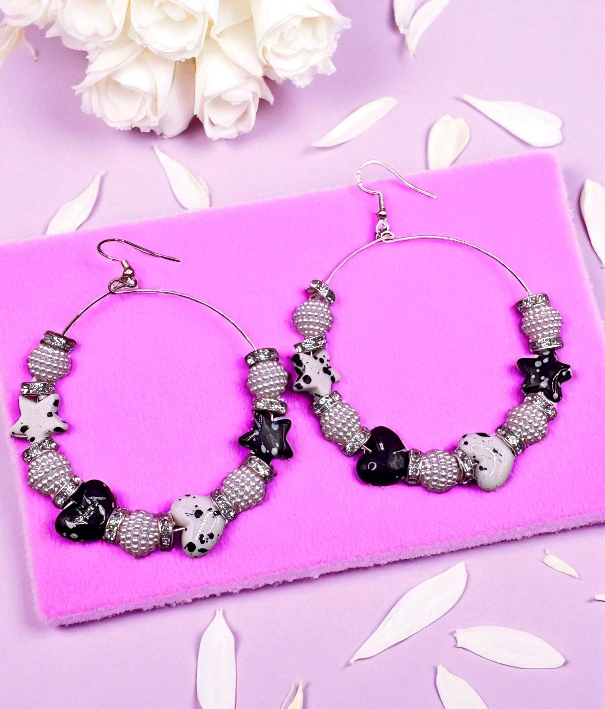 Hoop earrings with black and white bead design on a pink surface with white flowers.