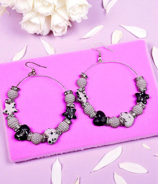 Hoop earrings with black and white bead design on a pink surface with white flowers.