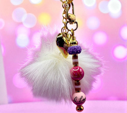 Keychain with fluffy white pom-pom and colorful beads on a pink blurred background