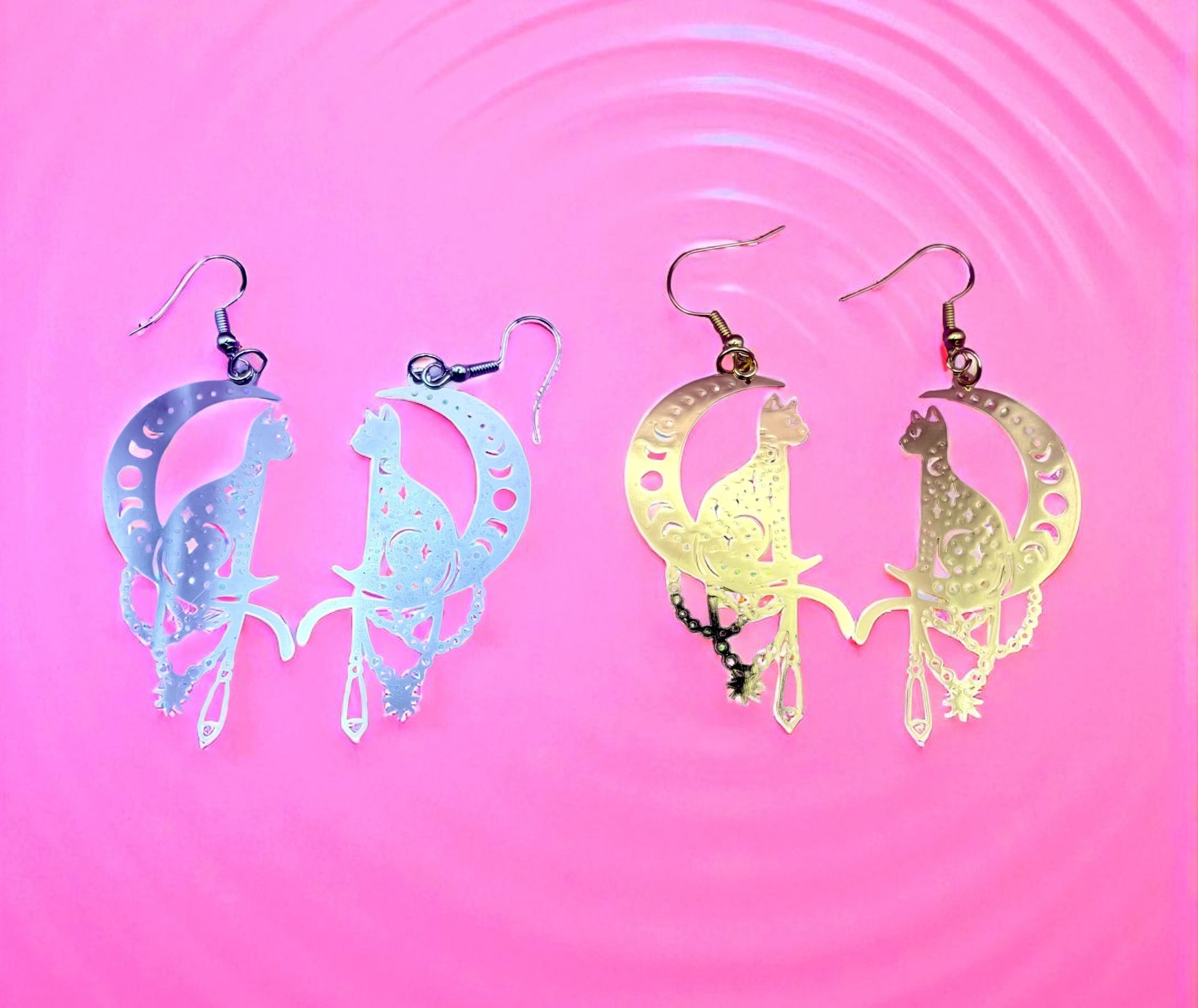 Two pairs of cat-shaped earrings on a pink background