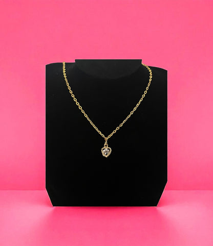 Gold necklace with a heart-shaped pendant on a black stand against a pink background