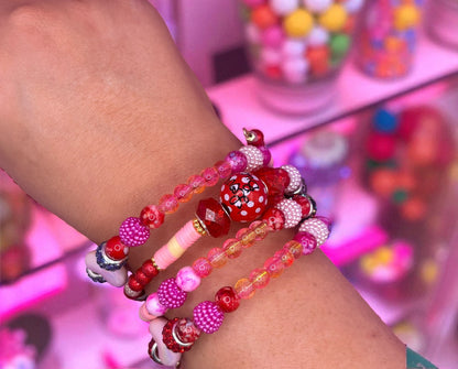 Close-up of a wrist wearing multiple colorful beaded bracelets with a blurred gumball machine in the background.