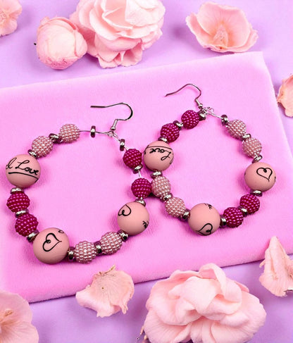 Pair of beaded earrings on a pink surface with flowers around