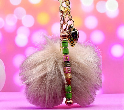 Fuzzy keychain with colorful beads and charms against a pink blurred background