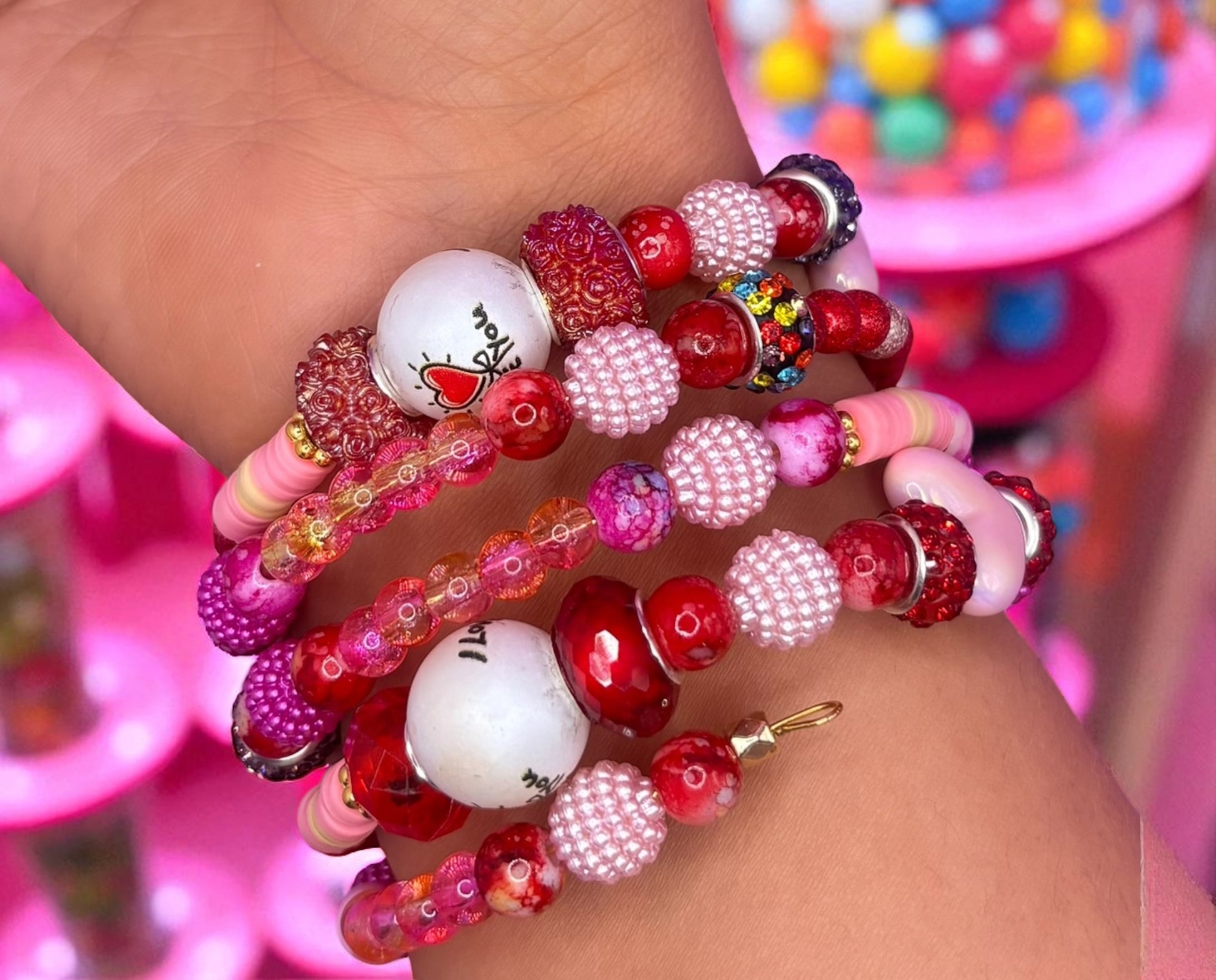 Colorful beaded bracelets on a wrist with a pink and multicolored background