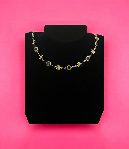 Necklace with floral and circular designs on a black stand against a pink background