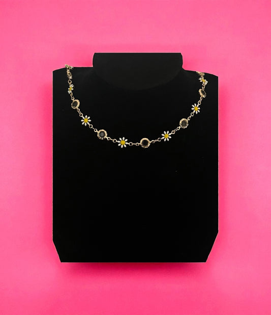 Necklace with floral and circular designs on a black stand against a pink background