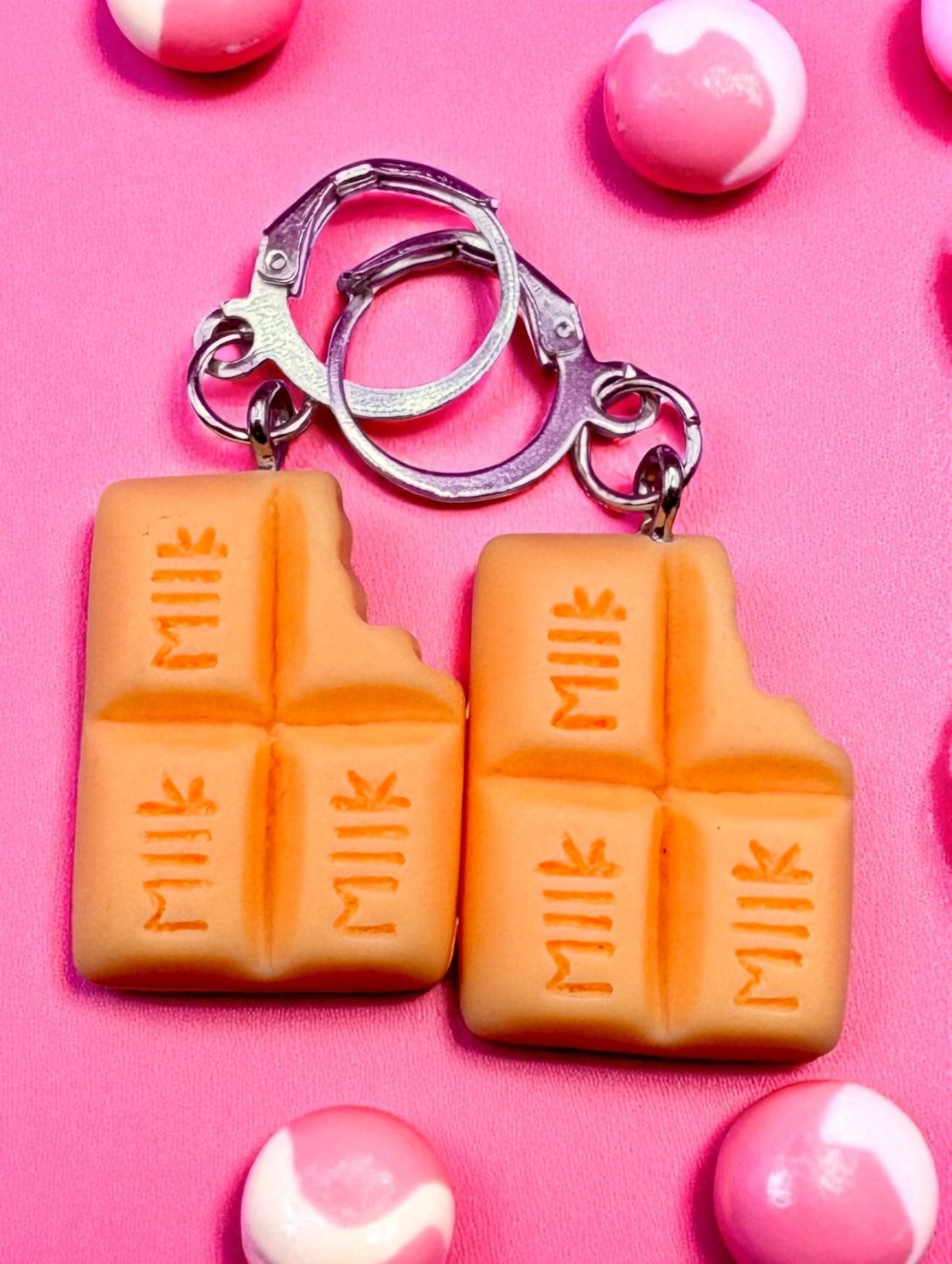 Two orange milk chocolate bar  earrings on a pink background with candy accents.