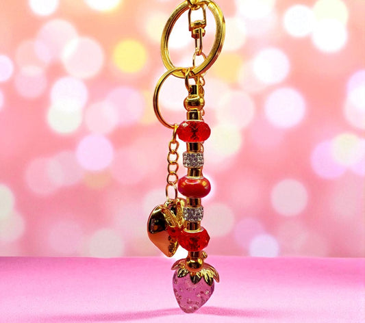 Decorative keychain with strawberry charm on a pink background