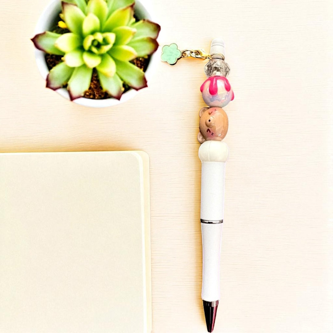 Decorative pen with a small figurine and beads on a light background