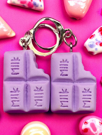 Purple milk chocolate bar  earrings on a pink background with colorful nail art.