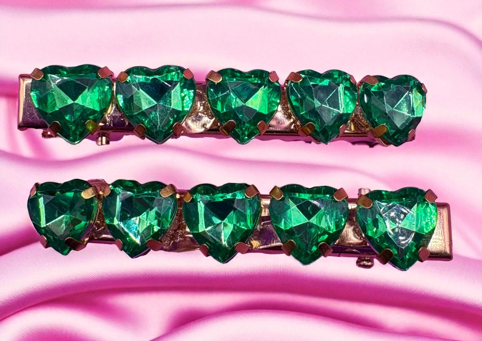 Two green heart-shaped gemstone hair clips on a pink fabric background