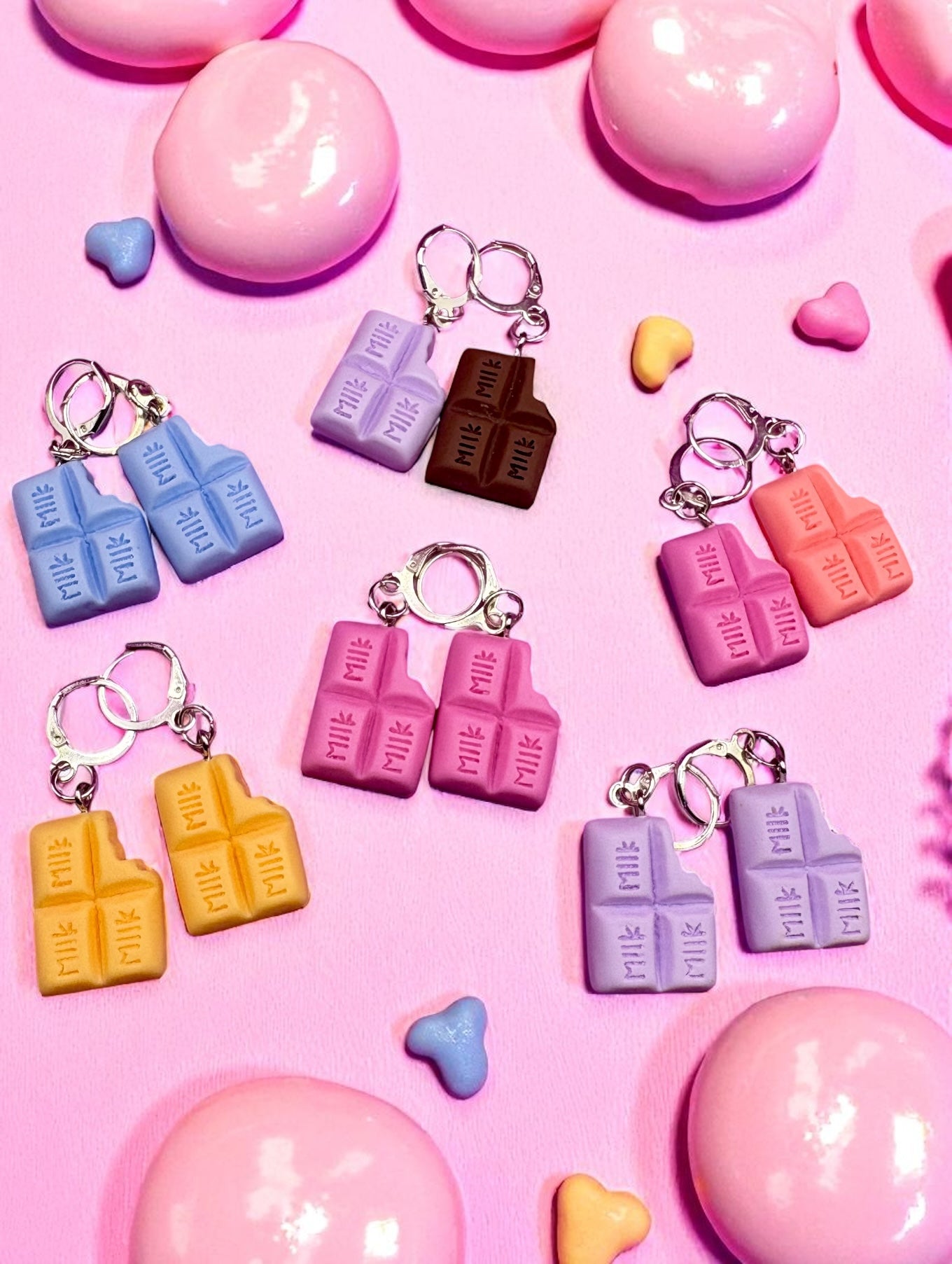 Colorful chocolate bar  earrings on a pink background with heart shapes.