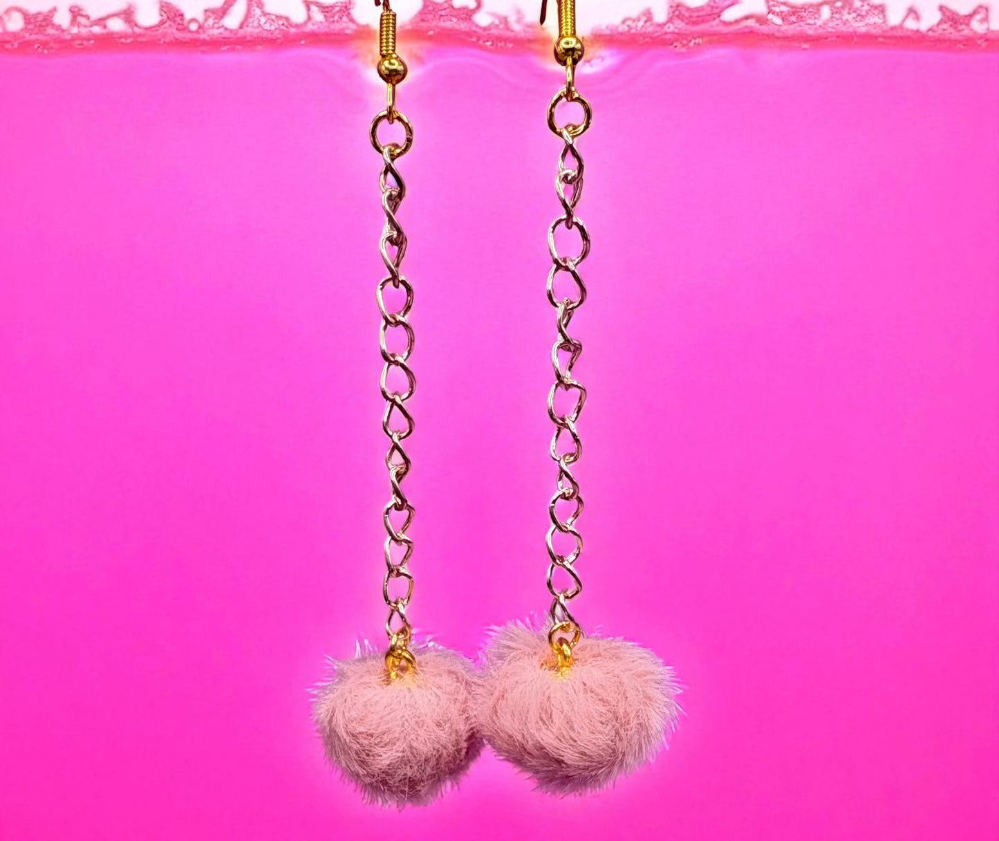 Pink pom-pom earrings with gold chains on a pink background