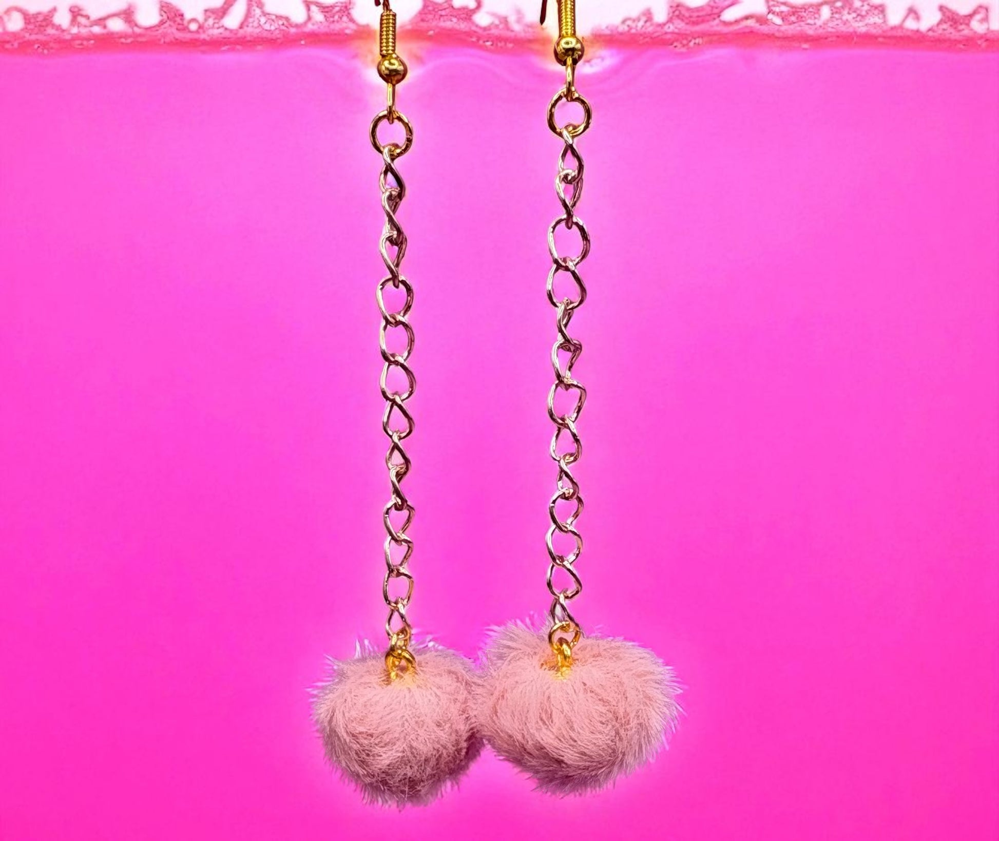 Pink pom-pom earrings with gold chains on a pink background