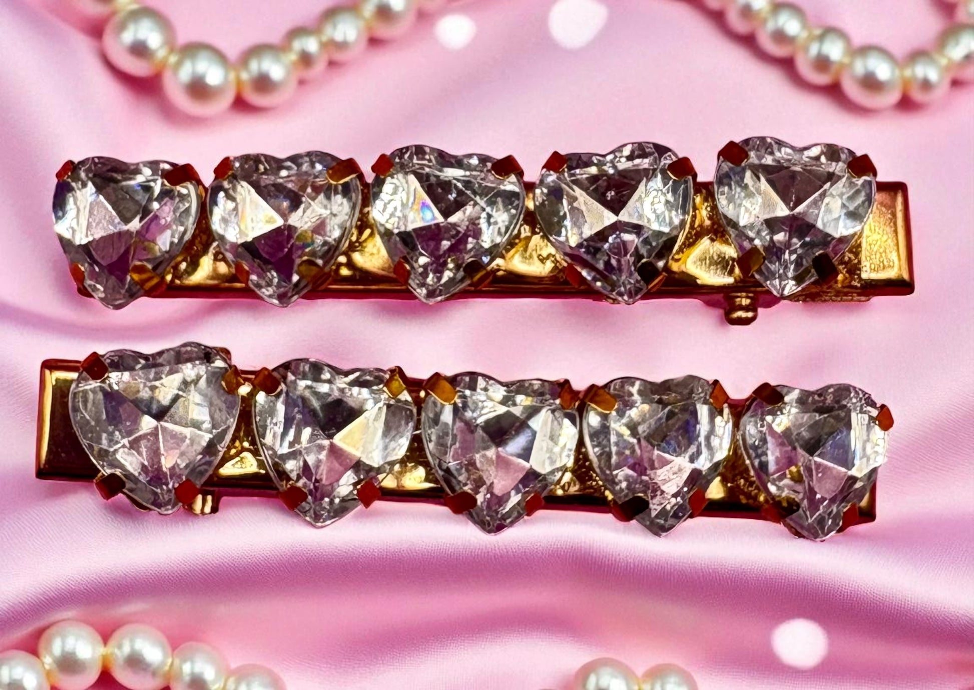 Two gold hair clips with heart-shaped crystals on a pink background