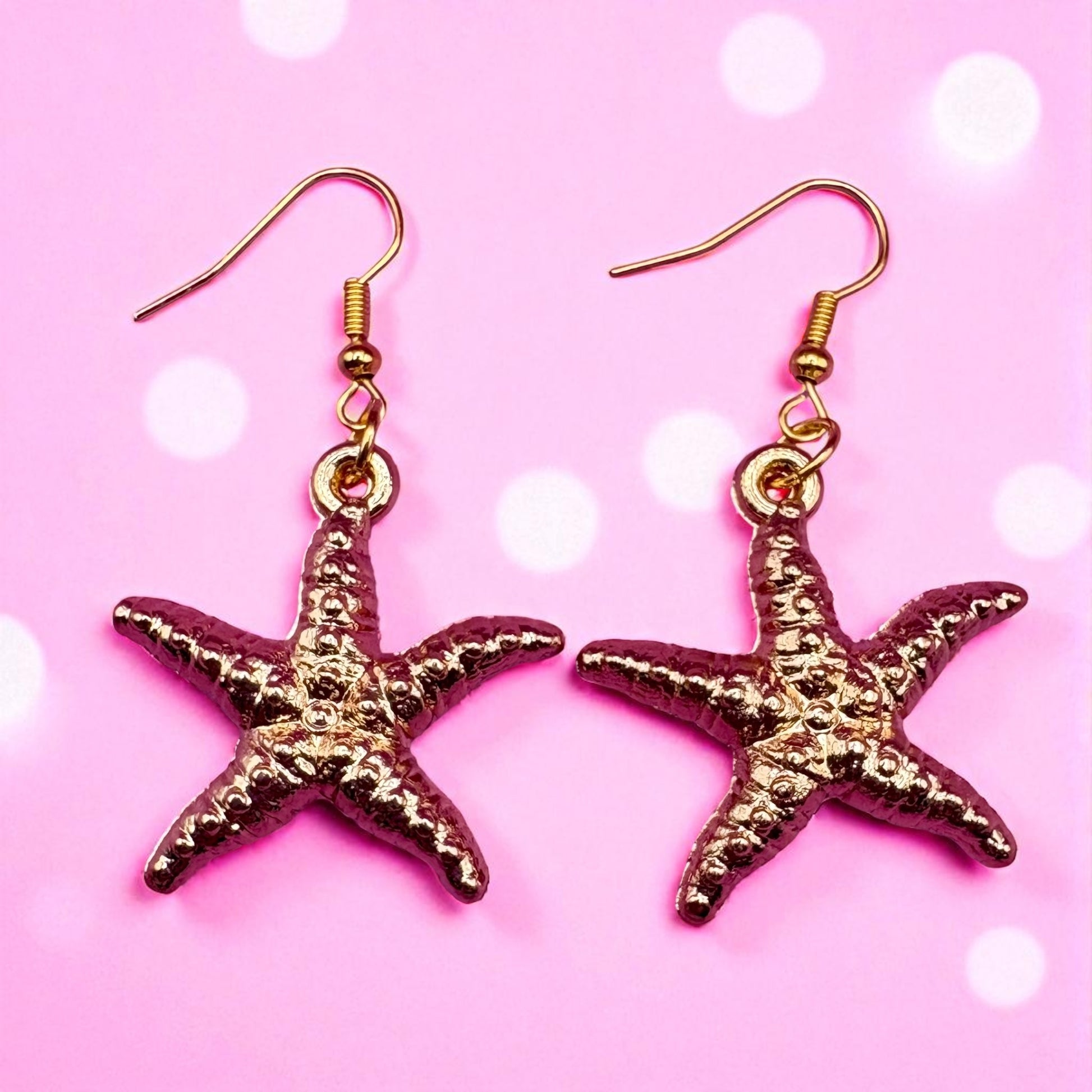 Gold starfish earrings on a pink background with white dots