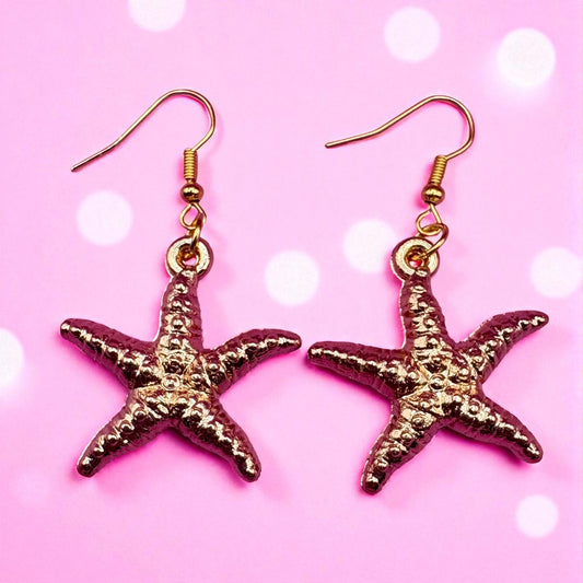 Gold starfish earrings on a pink background with white dots