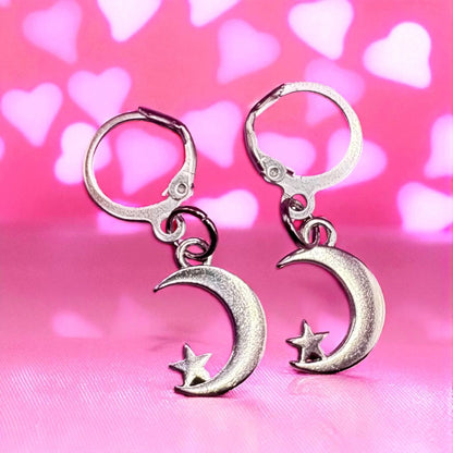 Silver moon and star earrings on a pink background with heart shapes