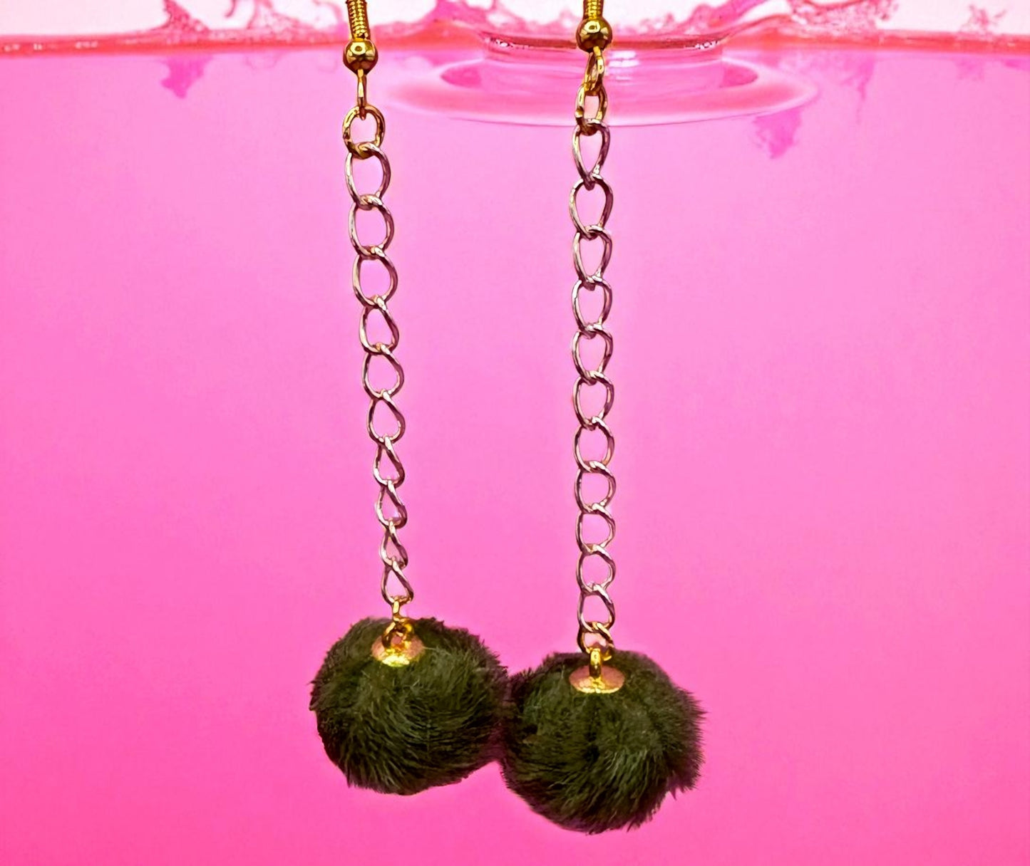 Green pom-pom earrings with gold chains on a pink background