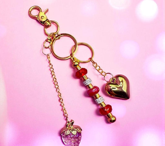 Decorative keychain with heart and strawberry charms on a pink background