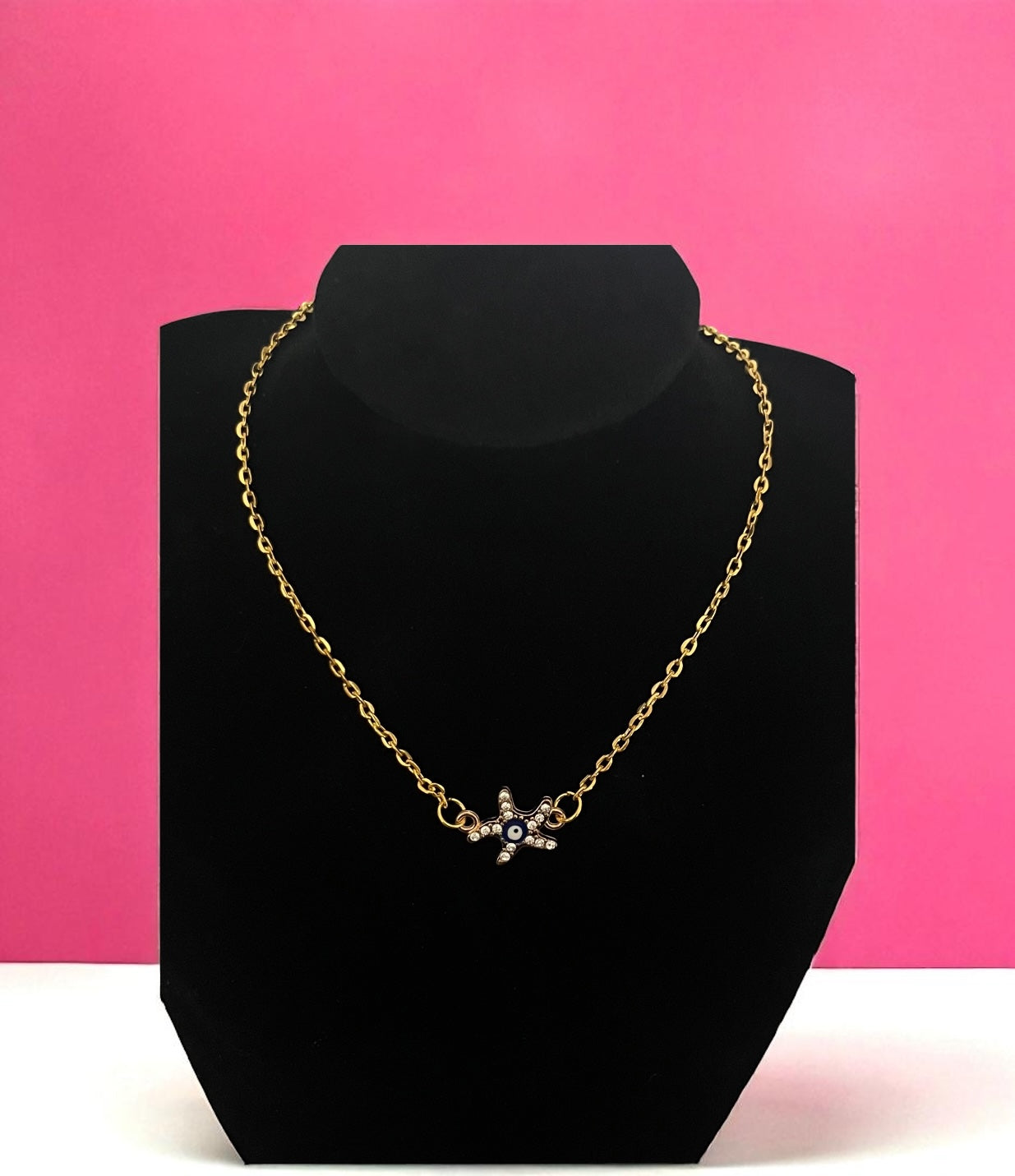 Gold necklace on a black bust against a pink background