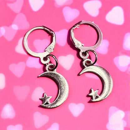 Silver moon and star earrings on a pink background with heart shapes