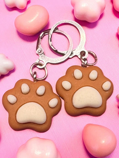 Paw-shaped k earrings on a pink background with heart-shaped objects