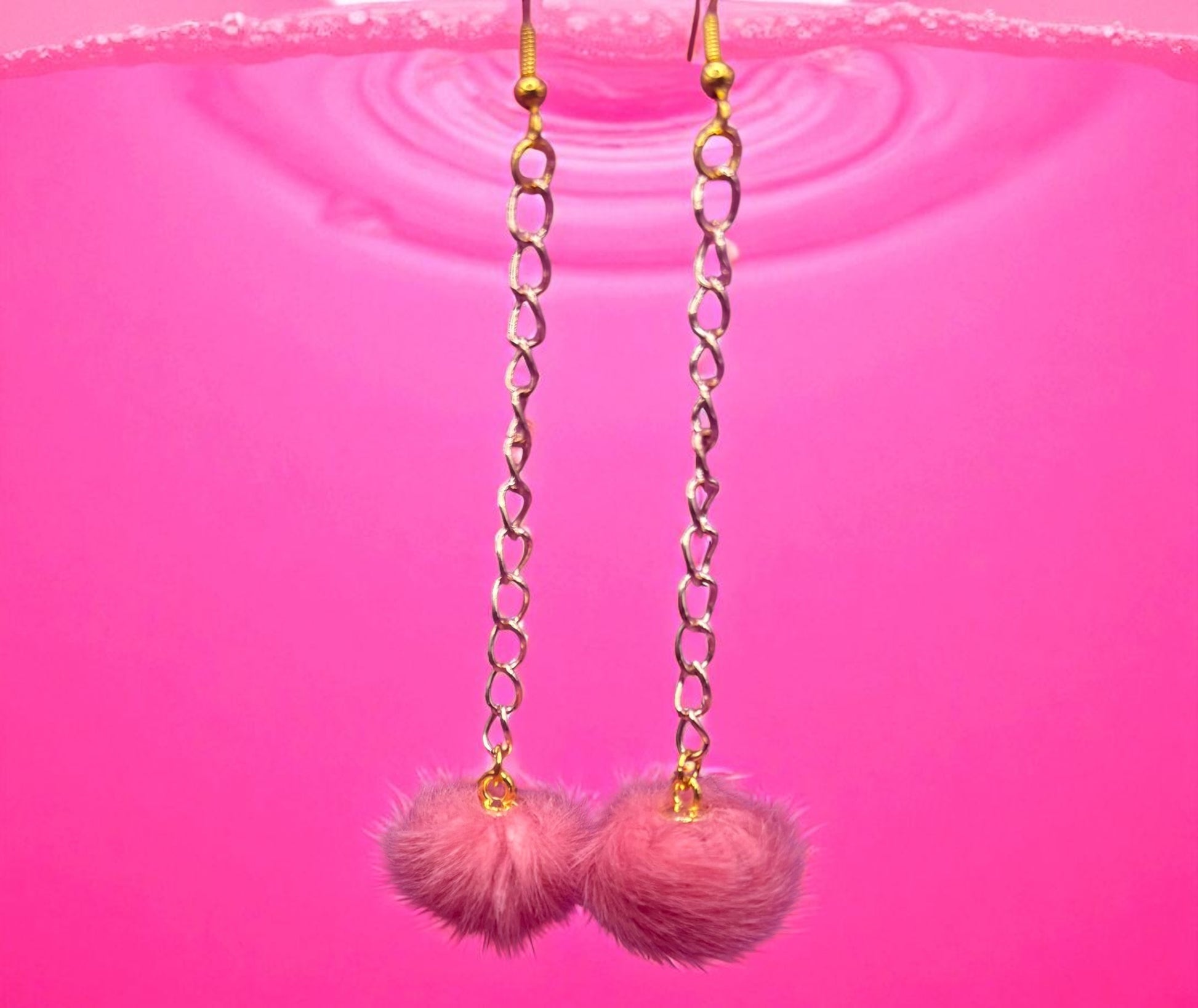 Pink pom-pom earrings with gold chains on a pink background
