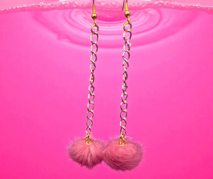 Pink pom-pom earrings with gold chains on a pink background
