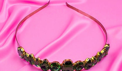 Decorative headband with green and gold stones on a pink satin background