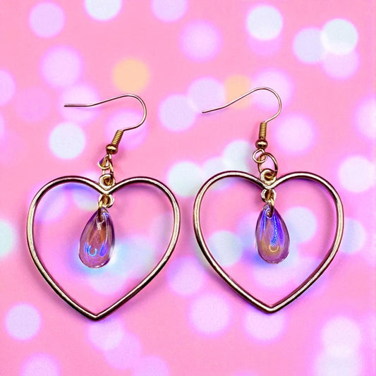 Heart-shaped earrings with purple teardrop charms on a pink background