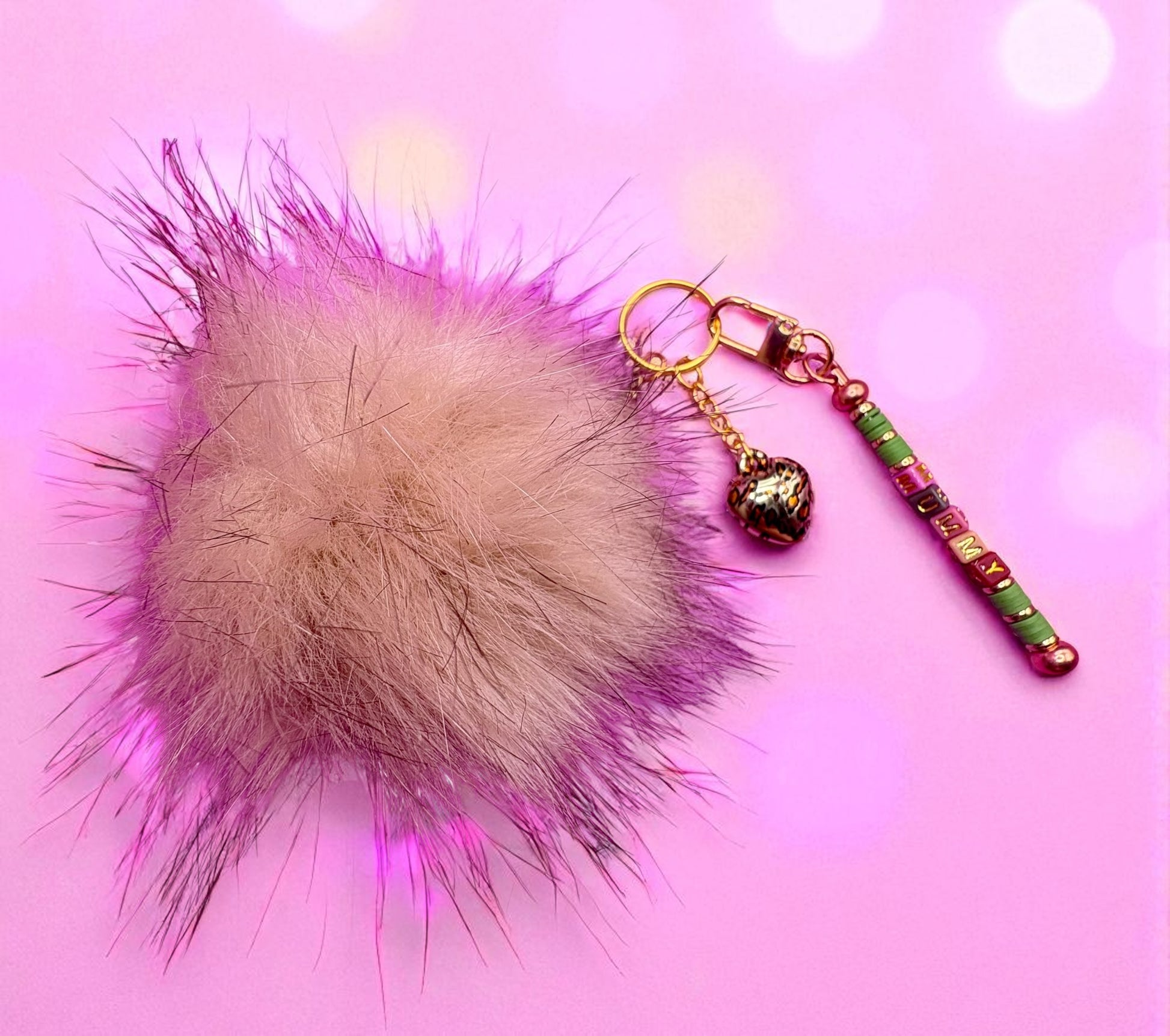 Fuzzy pom-pom keychain with decorative beads on a pink background