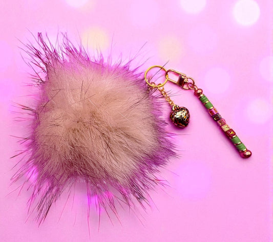 Fuzzy pom-pom keychain with decorative beads on a pink background