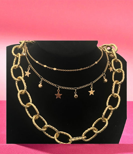 Gold chain necklace with star pendants on a black stand against a pink background