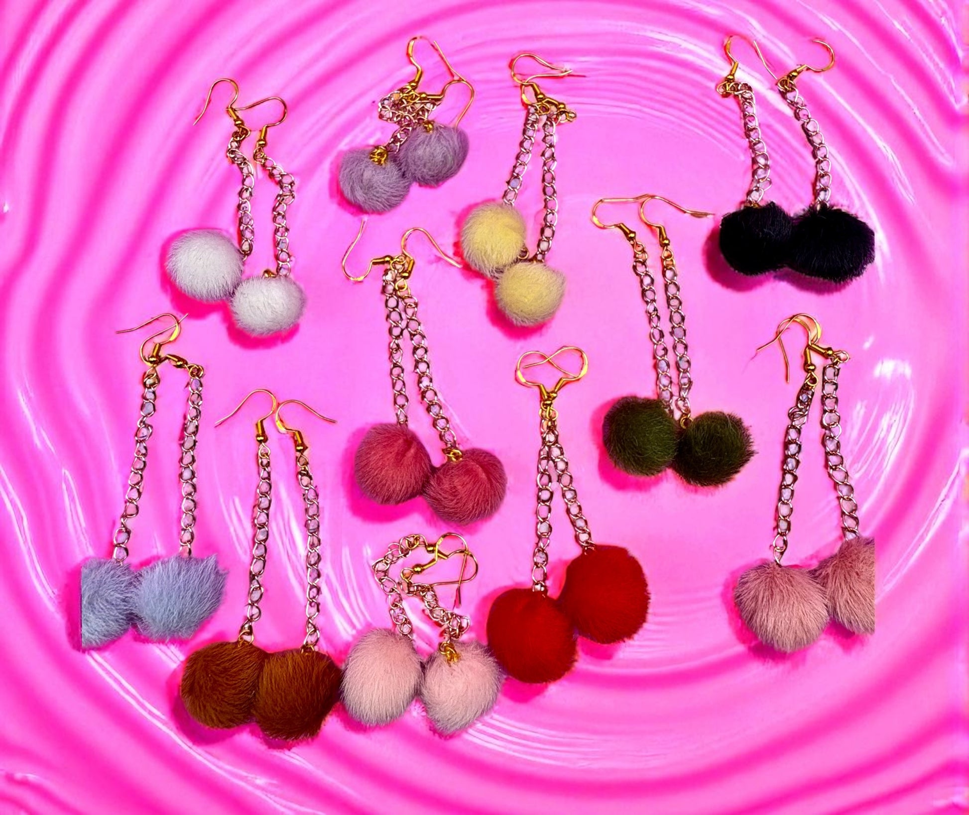 Colorful pom-pom earrings on a pink textured background