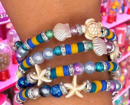 Colorful beaded bracelets with shell and starfish designs on a person's wrist.