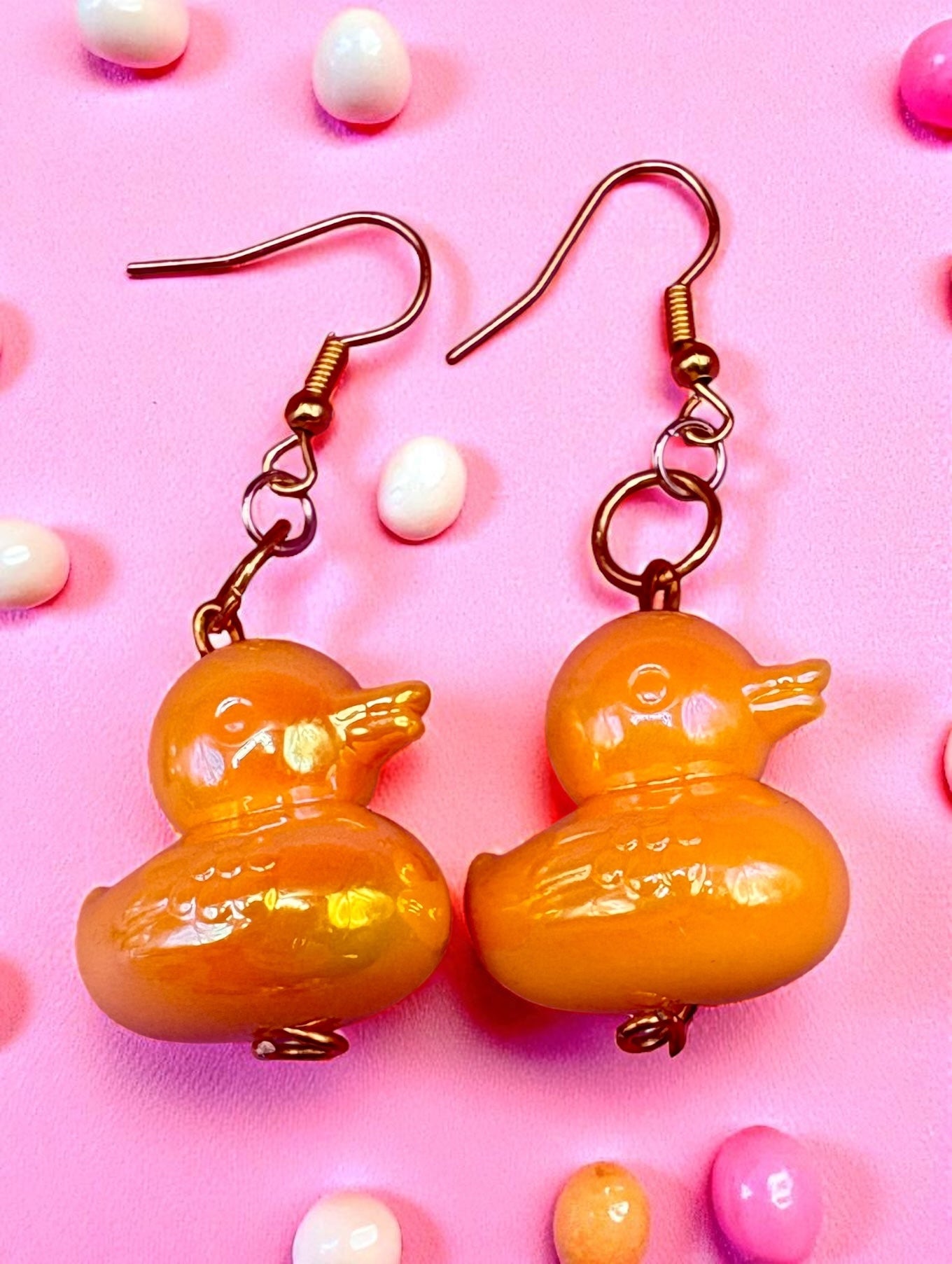 Yellow duck-shaped earrings on a pink background with pastel-colored beads.