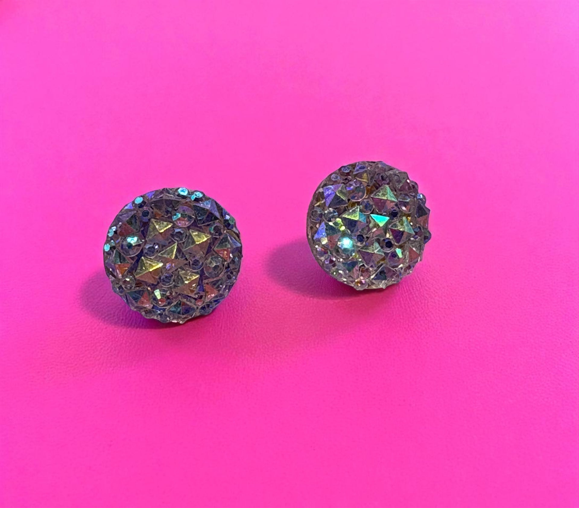 Pair of round, sparkling earrings on a pink background