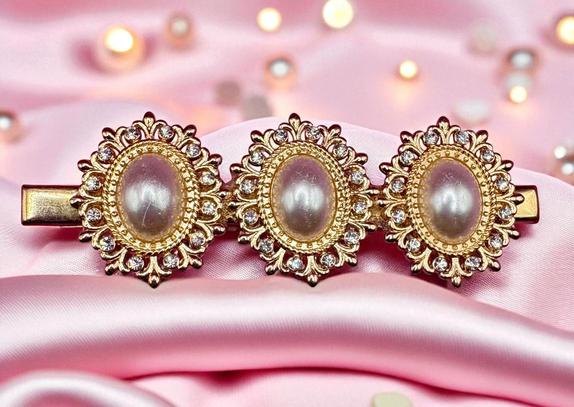 Three decorative hair clips with pearls and gold accents on a pink satin background.