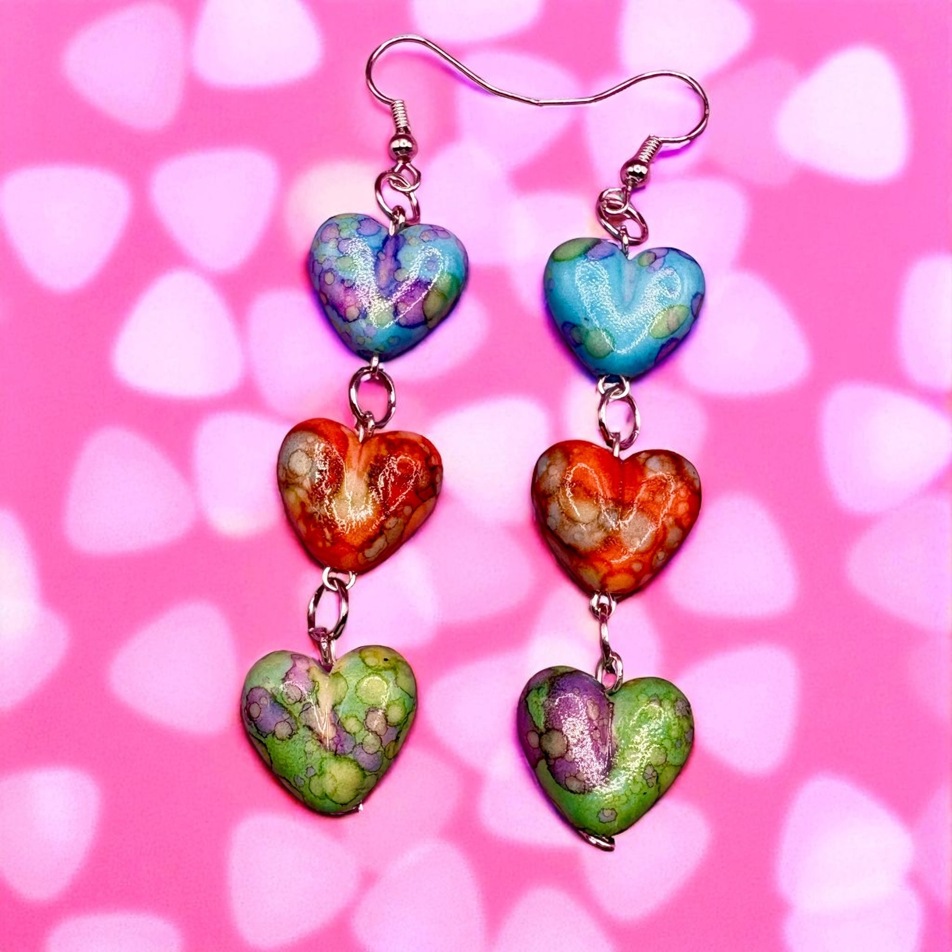 Colorful heart-shaped earrings on a pink background with heart patterns