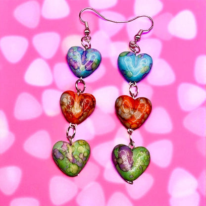 Colorful heart-shaped earrings on a pink background with heart patterns