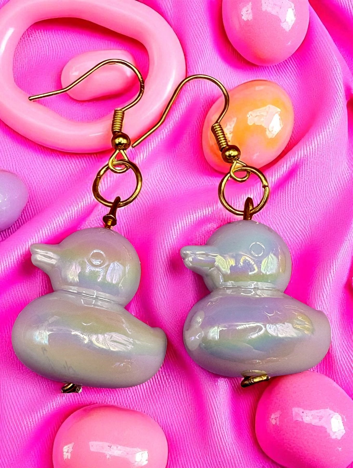 Pastel-colored duck-shaped earrings on a pink background