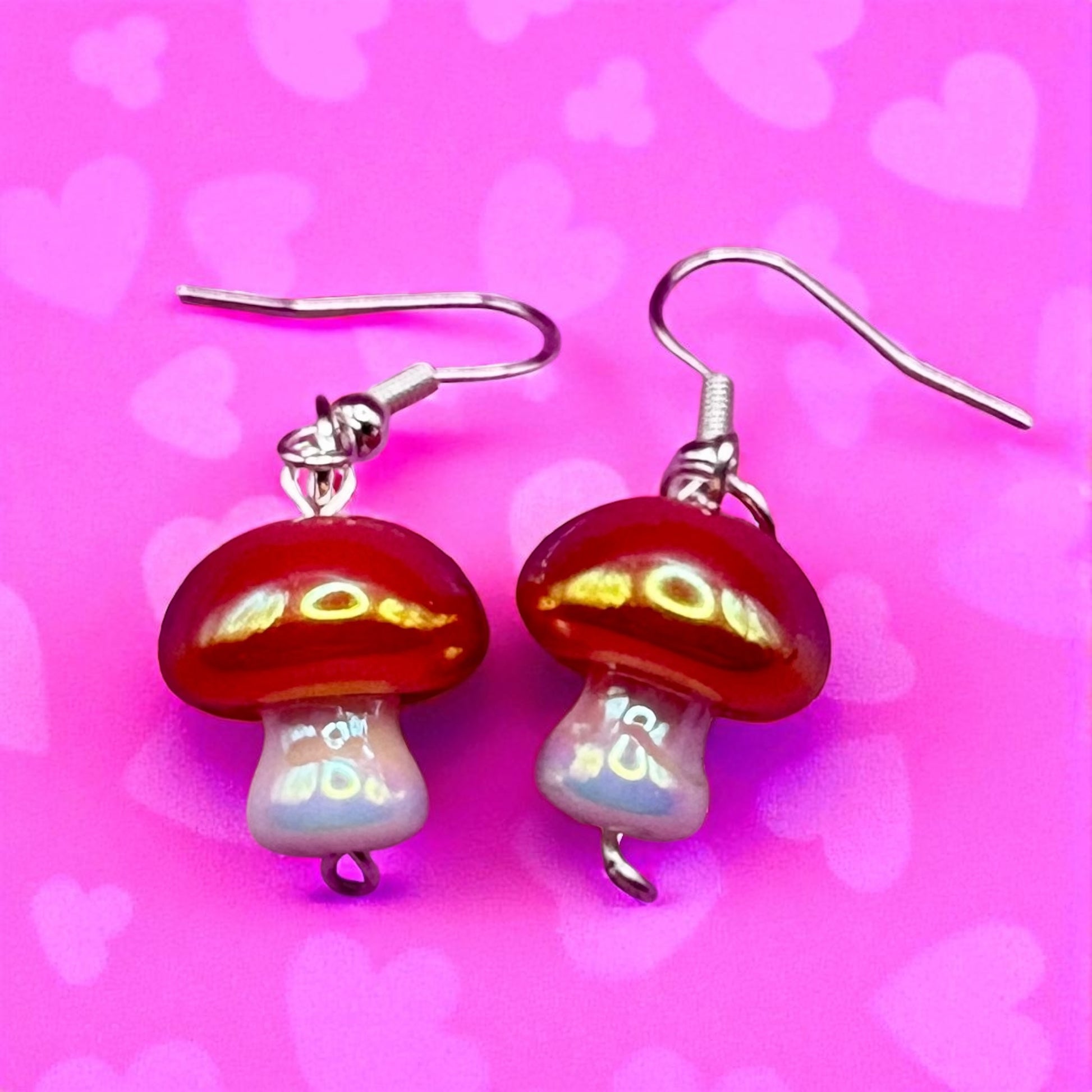 Red mushroom-shaped earrings on a pink background with heart shapes