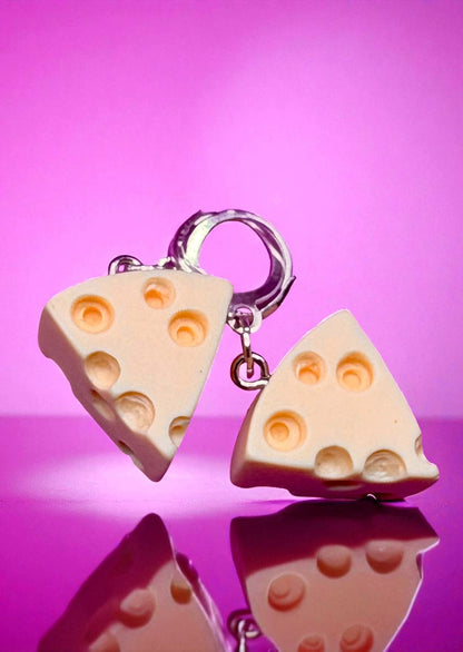 Cheese-shaped keychains on a reflective surface with a pink background