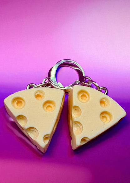 Two cheese-shaped keychains on a pink background
