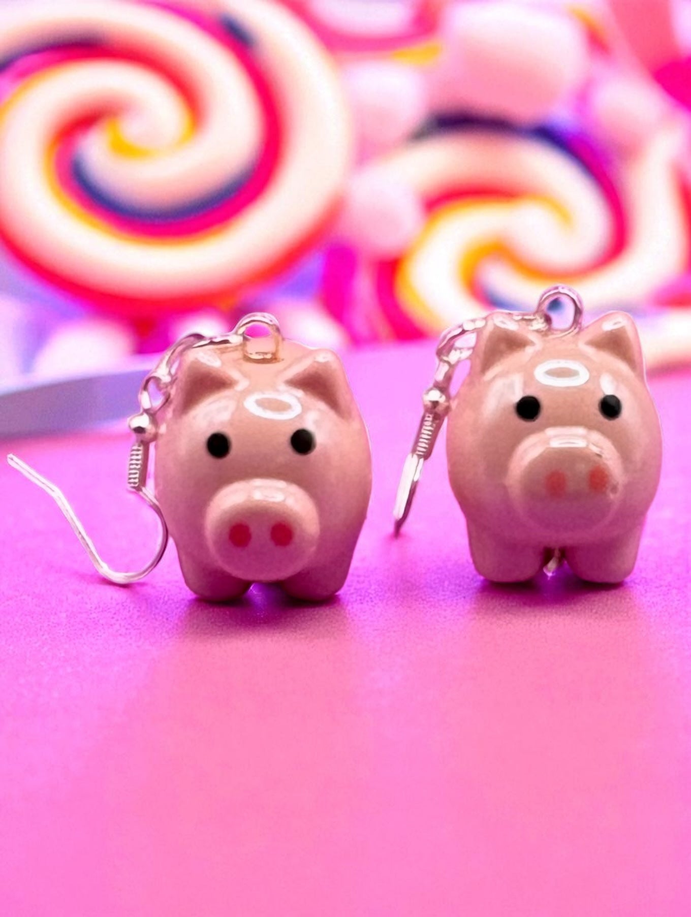 Two pink piggy bank  earrings on a pink background with colorful swirls.