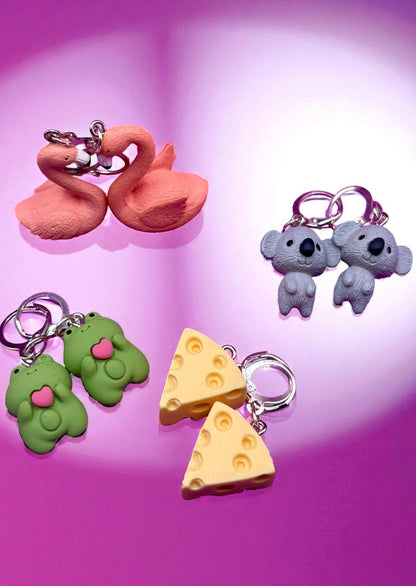 Set of colorful keychains including a swan, koalas, and cheese slices on a pink background