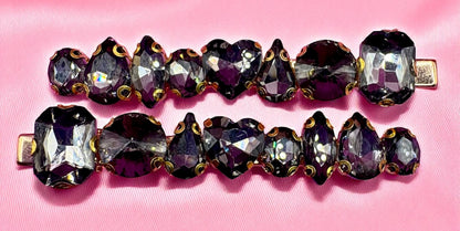 Pair of vintage-style jewelry clips with purple and clear gemstones on a pink background