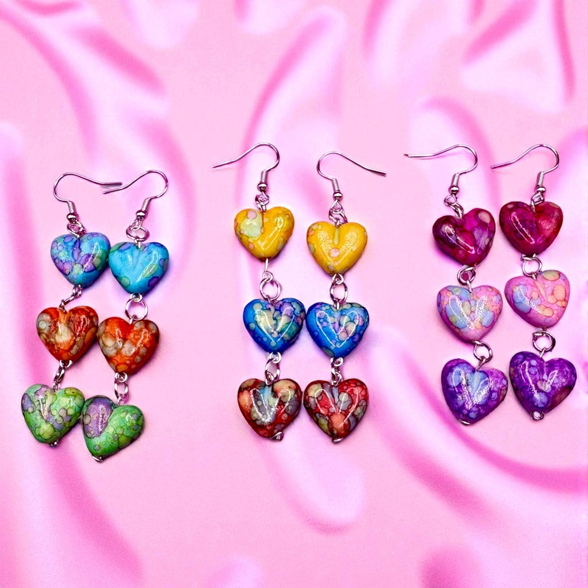 Colorful heart-shaped earrings on a pink fabric background